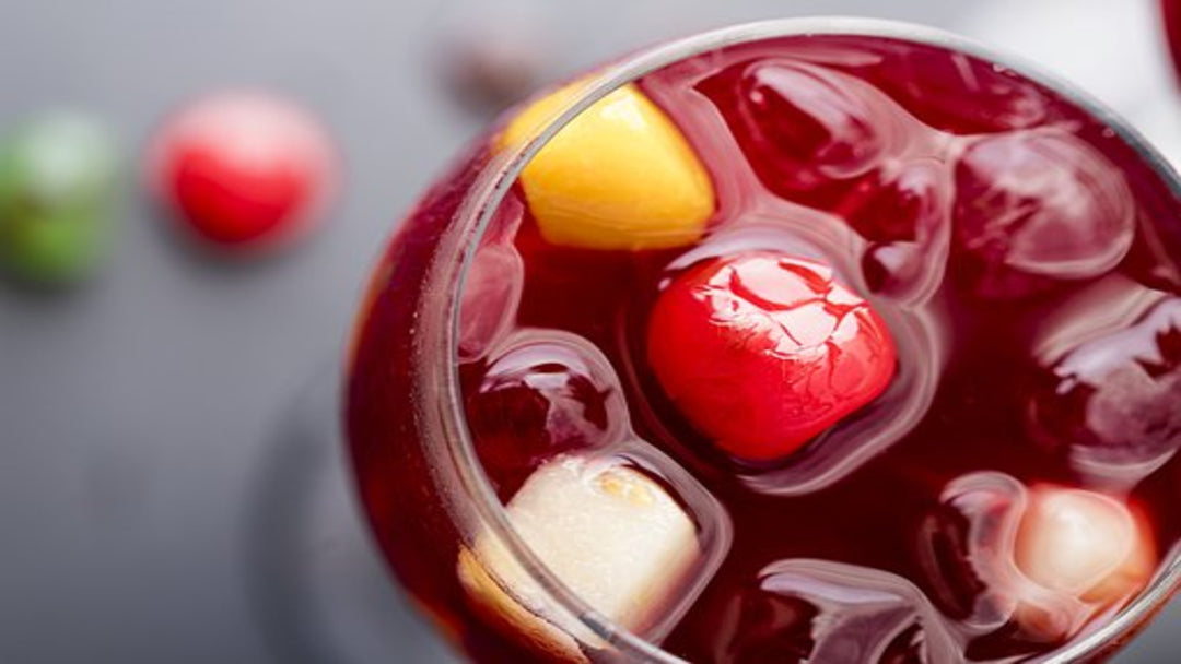 a glass of red sangria filled with fruit on a blue table